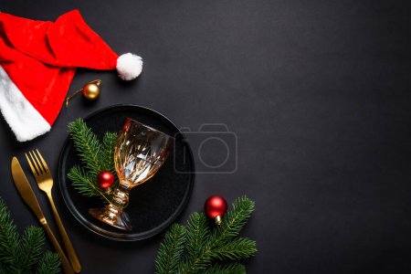 Photo for Christmas table setting with black plate, wine glass, golden cutlery and holidays decorations. Flat lay with space for text. - Royalty Free Image