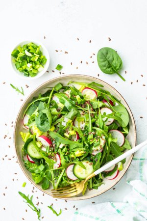 Photo for Green salad with spinach, arugula and radish with olive oil on white table. Top view with copy space. - Royalty Free Image