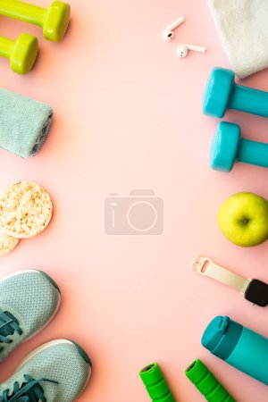 Photo for Healthy lifestyle and fitness concept. Sneakers, dumbbells, towel, green apple and fitness bracelet. Flat lay on pink. - Royalty Free Image