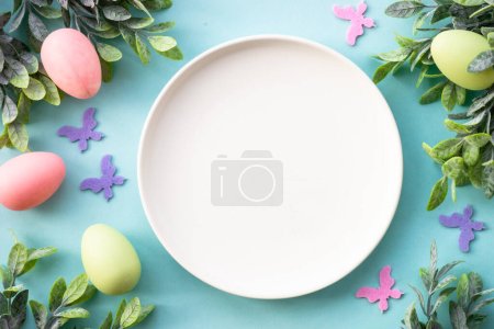 Foto de Mesa de Pascua, fondo de comida de Pascua. Plato blanco con huevos, flores de primavera, hojas verdes y mariposa. Puesta plana. - Imagen libre de derechos