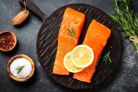 Photo for Raw fish at black table. Salmon fillet with lemon and spices. Flat lay. - Royalty Free Image