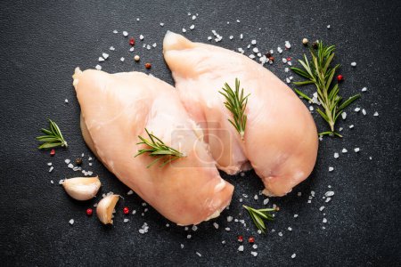 Téléchargez les photos : Poitrine de poulet non cuite avec épices à table noire. Vue du dessus. - en image libre de droit