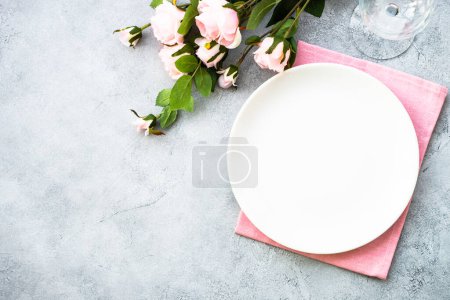 Téléchargez les photos : Cadre de table avec assiette blanche, couverts modernes et fleurs roses. Pose plate au blanc avec espace de copie. - en image libre de droit