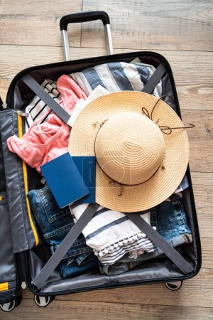 Photo for Open Suitcase with summer cloth, hat and passports. Travel concept. Flat lay image on wooden background. - Royalty Free Image