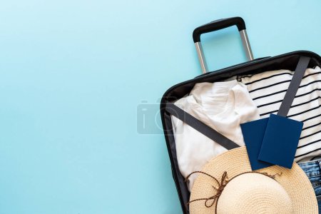 Photo for Open Suitcase with summer cloth, hat and passport on blue background. Flat lay image. - Royalty Free Image