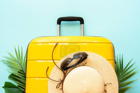 Photo for Summer holidays, traveling concept. Suitcase, hat and palm leaves on blue background. Flat lay with space for text. - Royalty Free Image