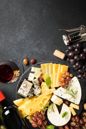 Téléchargez les photos : Assiette au fromage et vin rouge. Fromage artisanal serti de raisin sur planche d'ardoise. Vue du dessus au fond noir. - en image libre de droit