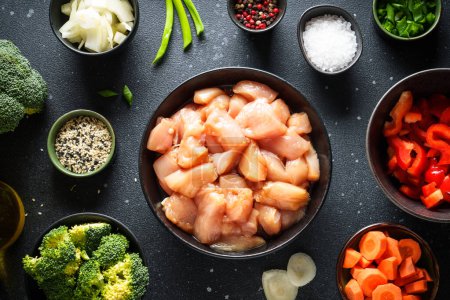 Téléchargez les photos : Préparation des aliments asiatiques. Poulet en sauce soja, paprika, brocoli et oignon sur fond noir. Nourriture crue, ingrédients pour la recette. - en image libre de droit