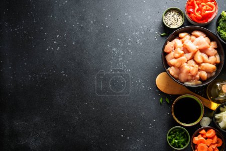 Foto de Pollo salteado con salsa de soja y verduras en el fondo negro. Ingredientes para cocinar, receta. Piso con espacio de copia. - Imagen libre de derechos
