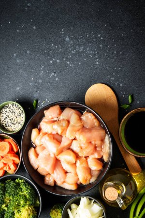 Téléchargez les photos : Préparation des aliments asiatiques. Poulet en sauce soja, paprika, brocoli et oignon sur fond noir. Nourriture crue, ingrédients pour la recette. Vertical. - en image libre de droit