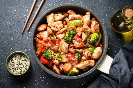 Foto de El pollo se fríe con verduras y sésamo en el fondo negro. Cocina tradicional asiática. - Imagen libre de derechos