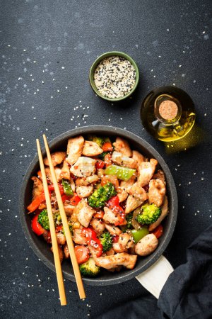 Téléchargez les photos : Faire revenir le poulet avec les légumes et le sésame sur fond noir. Cuisine asiatique traditionnelle. - en image libre de droit
