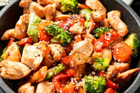 Téléchargez les photos : Remuer le poulet et les légumes et le sésame dans le wok. Cuisine asiatique. Gros plan. - en image libre de droit