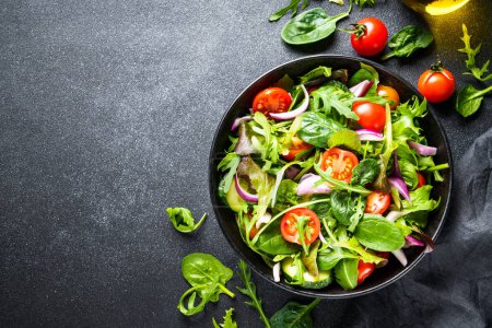 Photo for Salad in black bowl at dark background. Healthy green vegetable salad, diet menu. Top view. - Royalty Free Image