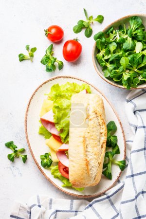 Foto de Sandwich de Ciabatta con lechuga, queso, tomate y jamón. Piso tendido sobre mesa blanca. - Imagen libre de derechos