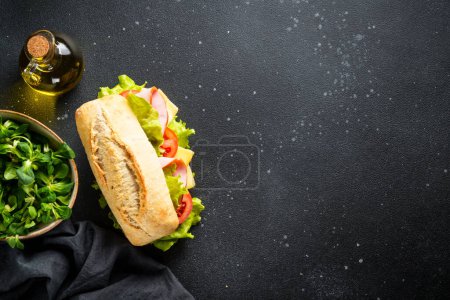 Foto de Sandwich con lechuga, queso, tomate y jamón sobre mesa de cocina negra con ingredientes. - Imagen libre de derechos