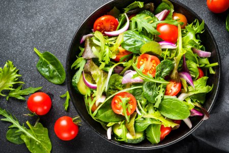 Téléchargez les photos : Salade dans un bol noir à fond sombre. Salade de légumes verts sains, menu diététique. Vue du dessus. - en image libre de droit