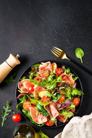 Téléchargez les photos : Salade verte sur fond noir. Salade fraîche avec confiture, feuilles de salade vertes et tomates. Vue du dessus avec espace pour le texte. - en image libre de droit