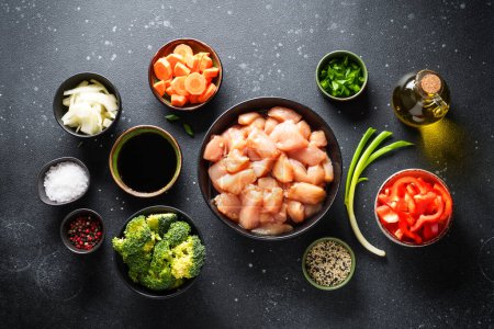 Photo for Chicken stir fry with soy sauce and vegetables at black background. Ingredients for cooking, recipe. Flat lay with copy space. - Royalty Free Image