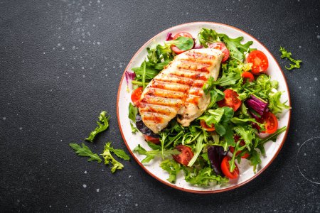 Téléchargez les photos : Salade verte avec poulet et légumes frais sur fond noir. Alimentation cétone, aliments sains. - en image libre de droit