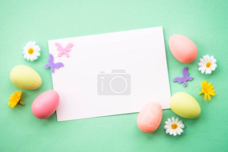 Téléchargez les photos : Carte de vœux de Pâques avec œufs, fleurs et papillons en arrière-plan de couleur. Image de pose plate avec espace de copie. - en image libre de droit