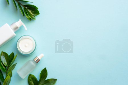 Téléchargez les photos : Produits cosmétiques naturels plat posé sur le bleu. Crème, savon et sérum aux feuilles vertes. - en image libre de droit