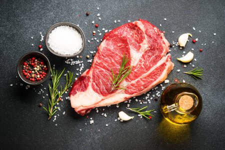Téléchargez les photos : Steak de viande crue avec des épices sur fond noir. Côtelette de boeuf. Pose TFlat. - en image libre de droit