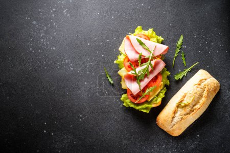 Photo for Ciabatta sandwich with lettuce, cheese, tomatoes and ham on black background. Fast food, snack or lunch. Top view with copy space. - Royalty Free Image