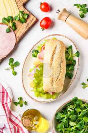 Téléchargez les photos : Sandwich à la ciabatta avec laitue, fromage, tomates et jambon. Restauration rapide, collation ou déjeuner. Vue de dessus sur blanc. - en image libre de droit