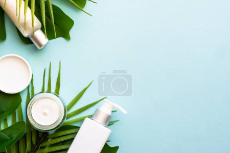 Téléchargez les photos : Cosmétique d'été, ensemble de produits cosmétiques avec des feuilles de palmier sur bleu. Vue supérieure avec espace de copie. - en image libre de droit
