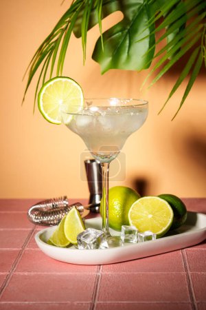 Foto de Margarita, cóctel alcohólico con lima, tequila de plata, cubitos de hielo y sal. Fondo tropical rosa. - Imagen libre de derechos