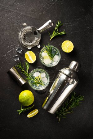 Téléchargez les photos : Gin tonique, cocktail traditionnel avec gin, tonique, glaçons, citron vert et romarin sur fond noir. Vue du dessus. - en image libre de droit