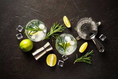 Téléchargez les photos : Gin tonic. Cocktail d'alcool avec gin, tonique, glaçons, citron vert et romarin sur fond noir. Vue supérieure avec espace de copie. - en image libre de droit