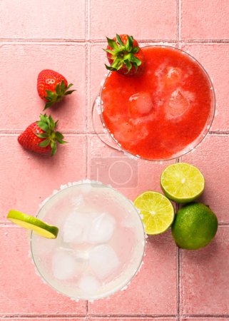 Foto de Cócteles Margarita. Margarita clásica y de fresa con tequila, hielo y lima con ingredientes al fondo de color. - Imagen libre de derechos