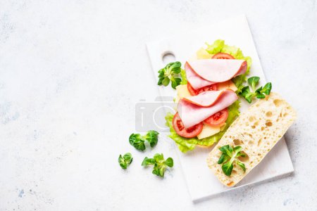 Téléchargez les photos : Sandwich à la laitue, fromage, tomates et jambon. Restauration rapide saine ou collation. Vue de dessus sur blanc. - en image libre de droit