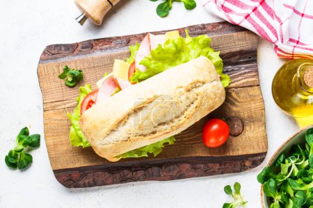 Photo for Ciabatta sandwich with lettuce, cheese, tomatoes and ham at cutting board. Fast food, snack or lunch. - Royalty Free Image