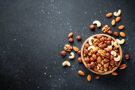 Photo for Nuts assortment at black background. Almond, hazelnut, cashew in wooden bowl. Flat lay with copy space. - Royalty Free Image