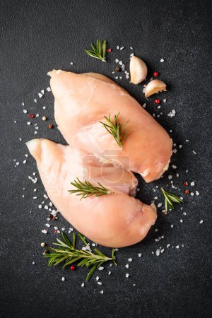 Téléchargez les photos : Viande de poulet. Poitrine de poulet cru avec des herbes et des épices sur fond noir. Vue de dessus, verticale. - en image libre de droit