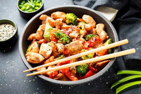 Téléchargez les photos : Faire revenir le poulet avec les légumes et le sésame sur fond noir. Cuisine asiatique traditionnelle. - en image libre de droit