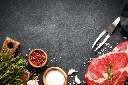 Téléchargez les photos : Steak de boeuf avec des épices sur fond noir. Ribeye steak viande crue. Vue supérieure avec espace de copie. - en image libre de droit