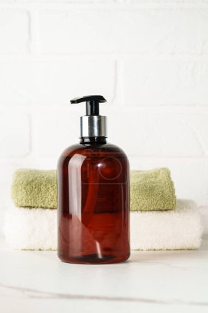Foto de Botella de jabón y pila de toallas sobre fondo de baño blanco. - Imagen libre de derechos