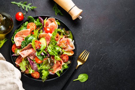Photo for Green salad on black background. Fresh salad with jamon, green salad leaves and tomatoes. Top view with space for text. - Royalty Free Image
