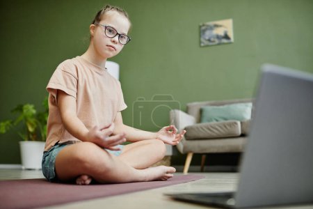 Téléchargez les photos : Portrait complet d'une adolescente atteinte du syndrome du duvet regardant une leçon en ligne sur le yoga à la maison, espace de copie - en image libre de droit