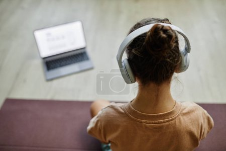 Photo for High angle view at child watching online lesson via laptop while practicing yoga at home, copy space - Royalty Free Image