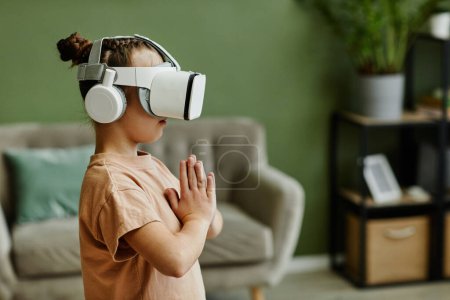 Photo for Side view portrait of tween girl practicing yoga workout in VR at home against green wall, copy space - Royalty Free Image