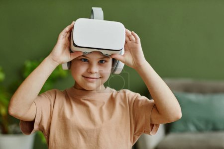 Foto de Waist up portrait of cute girl with down syndrome enjoying VR at home and looking at camera, copy space - Imagen libre de derechos