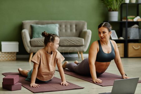 Photo for Portrait of young girl with down syndrome enjoying home workout with female instructor assisting - Royalty Free Image