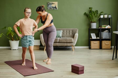 Photo for Full length portrait of young girl with down syndrome exercising indoors with female instructor assisting, copy space - Royalty Free Image