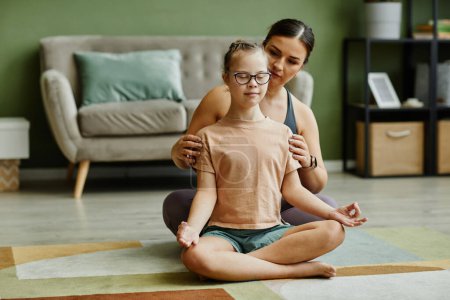 Photo for Portrait of female instructor assisting young girl with down syndrome doing yoga and meditating in fitness studio, copy space - Royalty Free Image