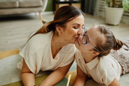 Photo for Portrait of loving mother kissing daughter with down syndrome while laying on floor together, non traditional family - Royalty Free Image